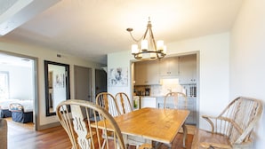A dining area with a wooden table and chairs, a chandelier, and a kitchen in the background. - Outpost: White Ridge A6 (Teton Village)