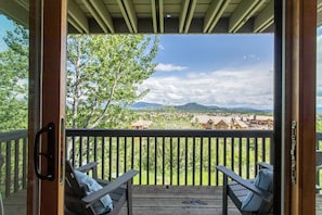 A wooden deck with two lounge chairs and a table, overlooking a scenic landscape with trees and distant buildings.