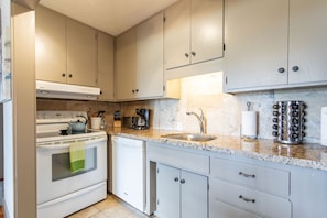 A kitchen with white cabinets, a stove, a dishwasher, a sink, and a coffee maker.