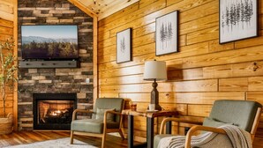 Una sala de estar acogedora con chimenea de piedra, paredes de madera, un televisor de pantalla plana y asientos cómodos.