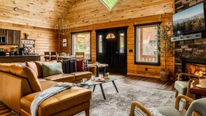 Interior acogedor de una cabaña con techo de madera, chimenea, sofá, mesa de centro y televisor.