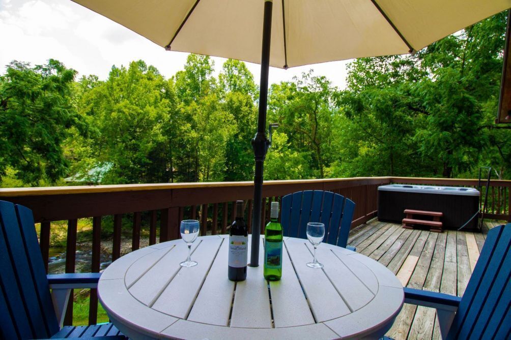 A wooden deck with a round table and chairs, a bottle of wine, and a glass on the table.