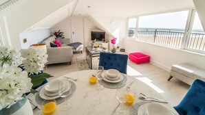 A dining area with a table set for four, a sofa, and a view of the beach. - Sea View Penthouse (Great Yarmouth)