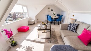 A modern loft apartment with a dining area, a sofa, and a small red ottoman. - Sea View Penthouse (Great Yarmouth)