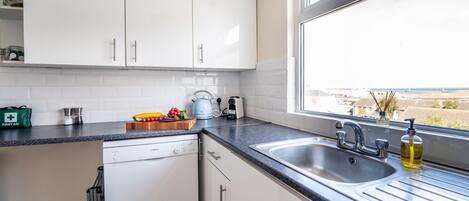 A modern kitchen with white cabinets, a dishwasher, a sink, and a window with a view of the city.