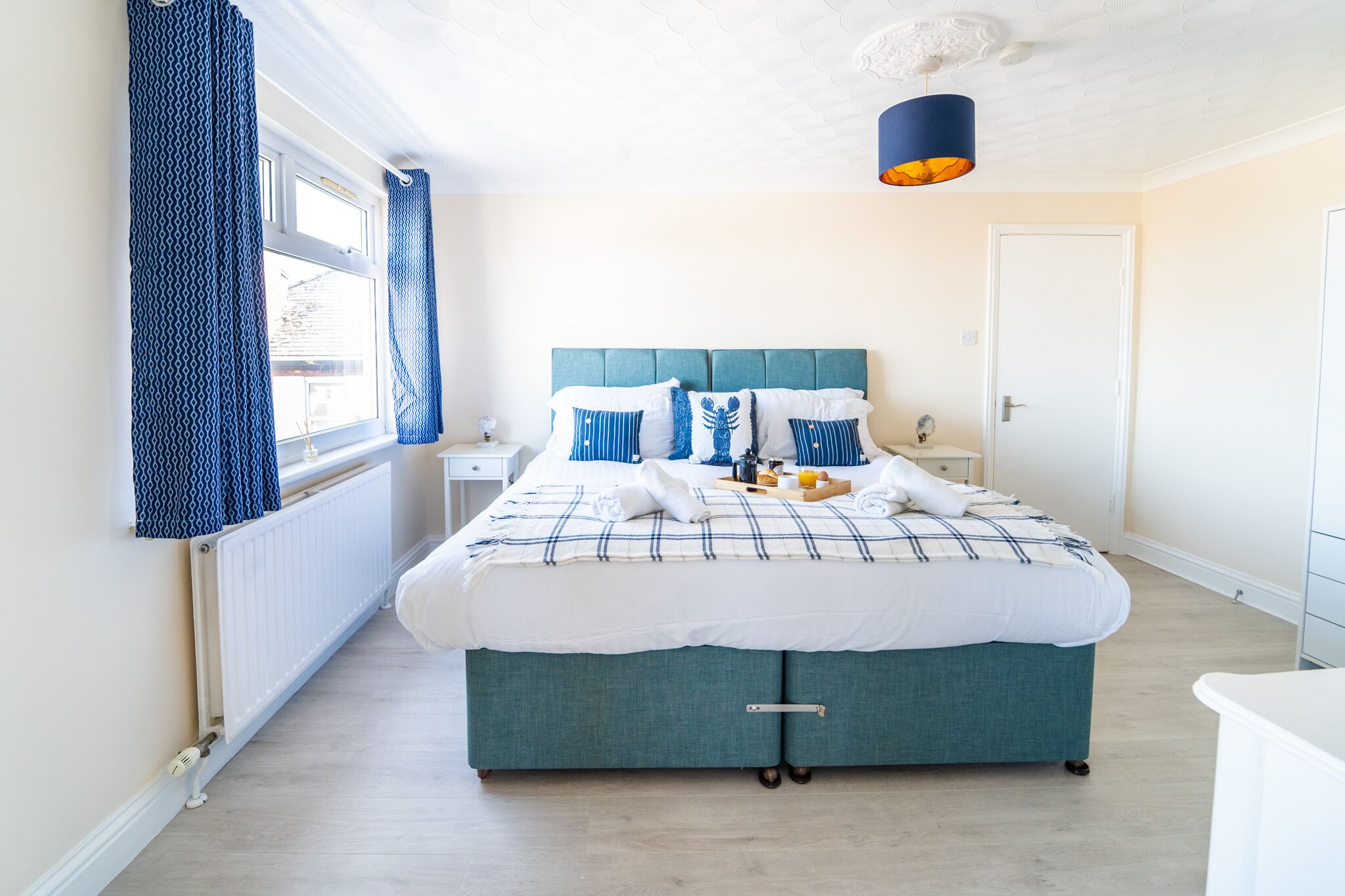 A bedroom with a bed, a bedside table, a window with curtains, and a ceiling light.