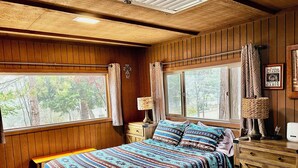 Un dormitorio tipo cabaña con una cama grande, paredes de madera y ventanas con vistas a un bosque.