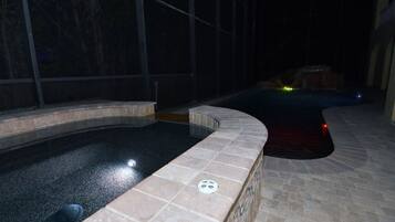Une piscine à bord incurvé, dotée d’une grille de vidange, entourée d’un sol carrelé et d’un mur en pierre.