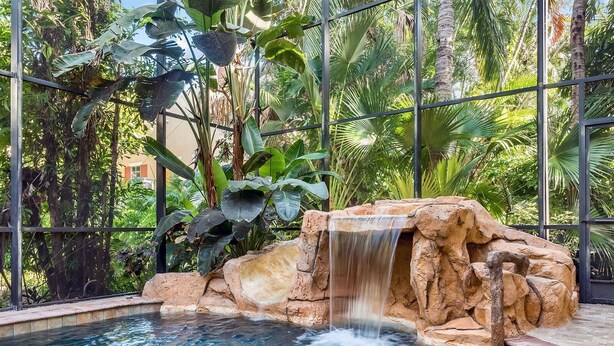 A pool with a waterfall feature surrounded by tropical plants and a metal fence. - Wiles Drive (Captiva)