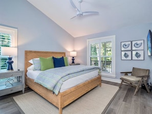 A bedroom with a wooden bed, a nightstand, a chair, a ceiling fan, and a window with blinds.