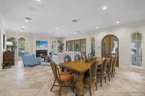 Un amplio comedor con una mesa y sillas de madera, una chimenea y grandes ventanas que ofrecen vistas al exterior.