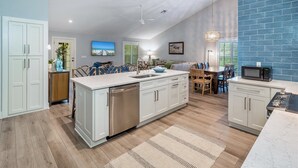 A modern kitchen with white cabinetry, a stainless steel dishwasher, and a blue brick accent wall. - Wiles Drive (Captiva)