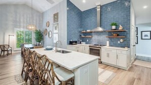 A modern kitchen with a large island, white cabinetry, and blue backsplash. - Wiles Drive (Captiva)