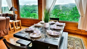 A dining table set for six with white plates and napkins, a vase of greenery, and a view of a forest through large windows. - Rustic Mountain Retreat ~ Panoramic Mountain View ~ Hot Tub ~ Game Room  (Sevierville)