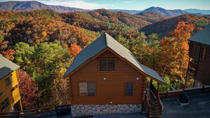 A log cabin with a stone foundation, a front porch, and a view of a forested mountain range. - Rustic Mountain Retreat ~ Panoramic Mountain View ~ Hot Tub ~ Game Room  (Sevierville)