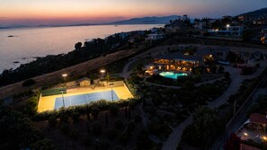 An aerial view of a coastal property with a tennis court, swimming pool, and residential buildings. - LYCIPONON VILLA for an unforgettable, relaxing, private, and secure vacation (Ανάβυσσος)