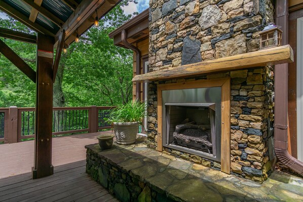 A stone fireplace with a wooden mantel, surrounded by a stone wall and a wooden deck.