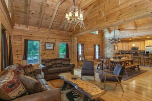 A spacious cabin interior with a dining area, kitchen, and a large window offering a view of the outdoors. - Mtn Lodge~Hot Tub+Fire Pit+Fireplace, WiFi! (Burnsville)