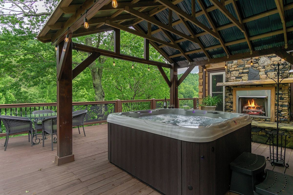 A hot tub on a wooden deck with a stone fireplace and a pergola overhead.