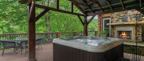 A hot tub on a wooden deck with a stone fireplace and a pergola overhead.