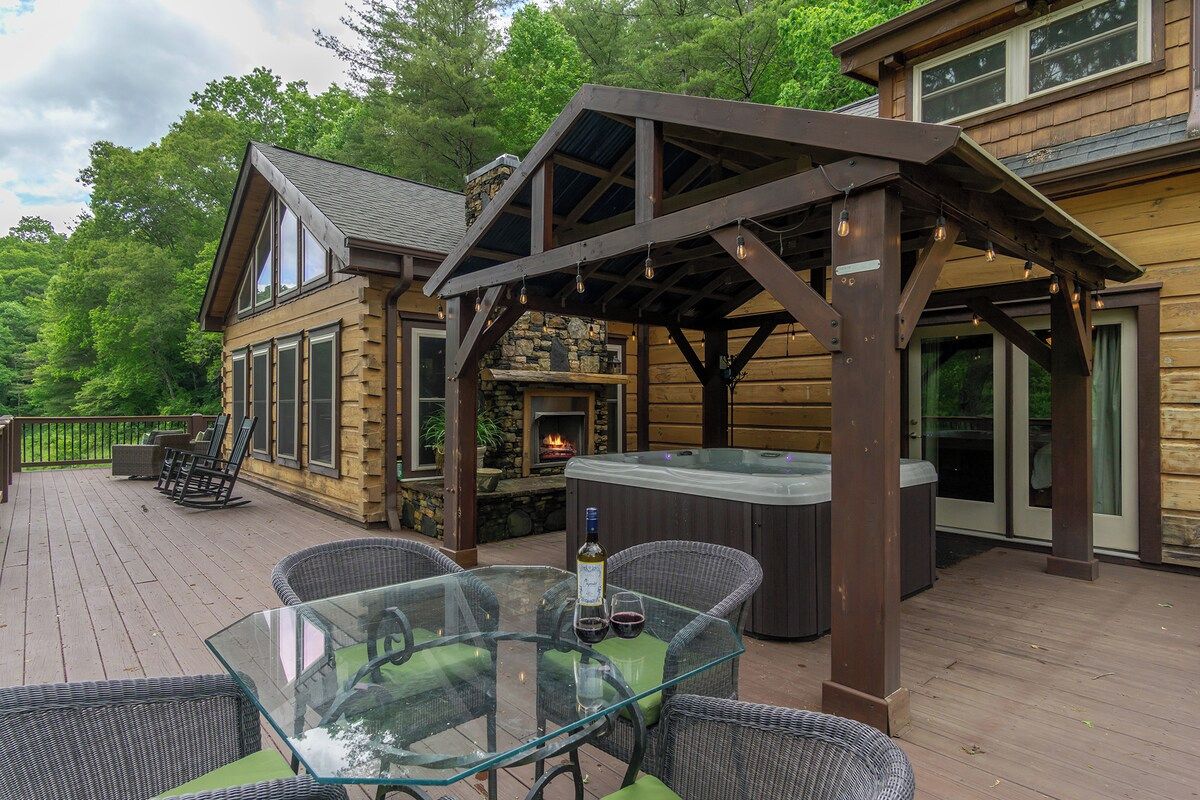 A wooden deck with outdoor seating, a hot tub, and a stone fireplace.