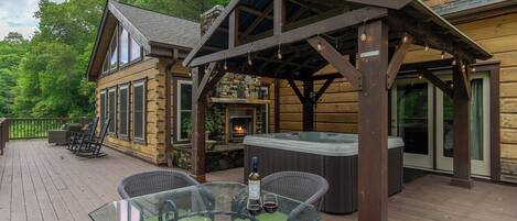 A wooden deck with outdoor seating, a hot tub, and a stone fireplace.
