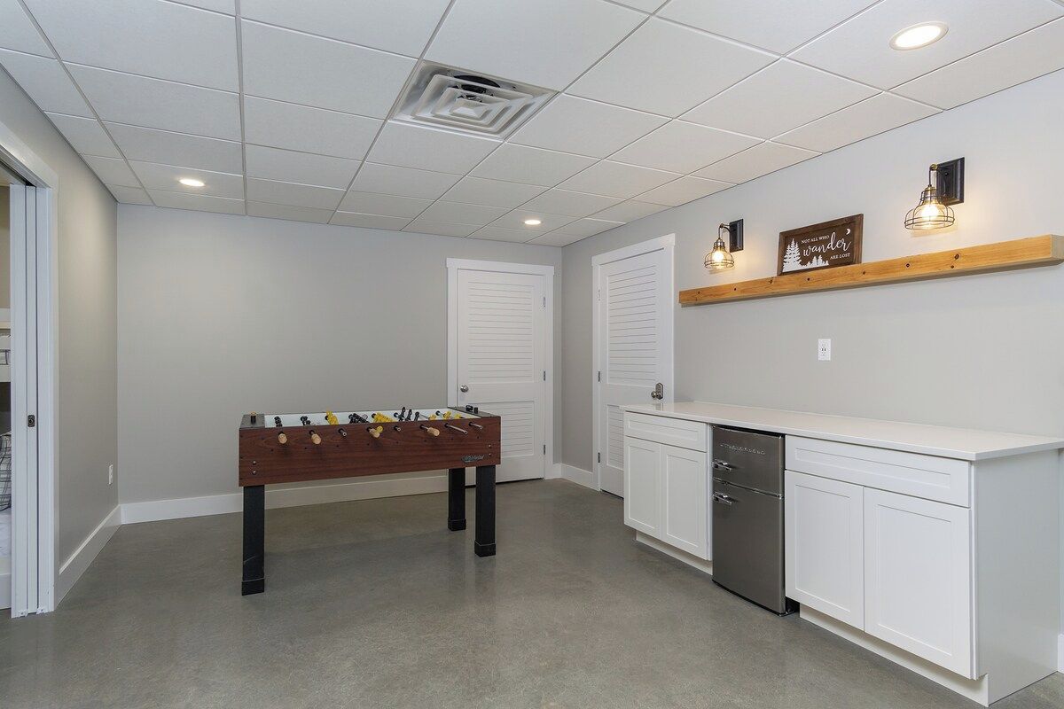 A clean, modern kitchen with a foosball table, white cabinetry, and a built-in dishwasher.