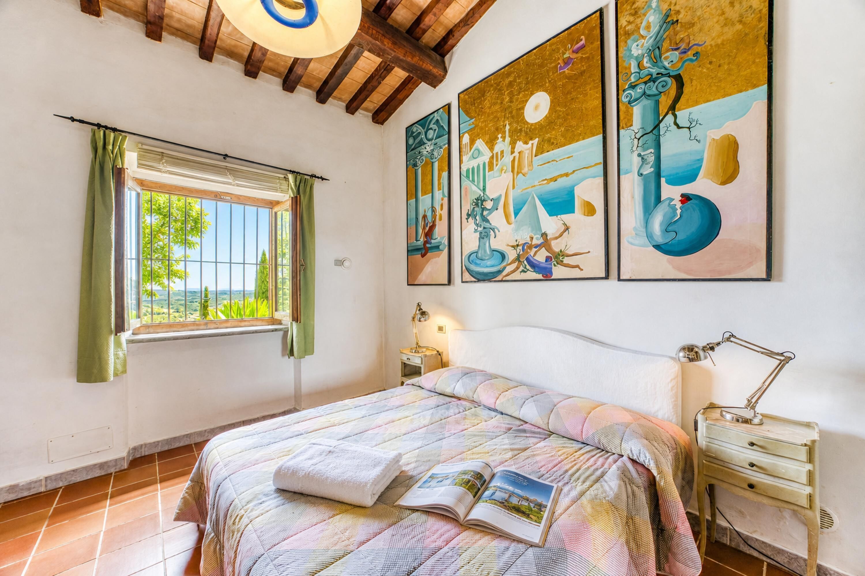 A bedroom with a bed, a window, a nightstand, and wall art.