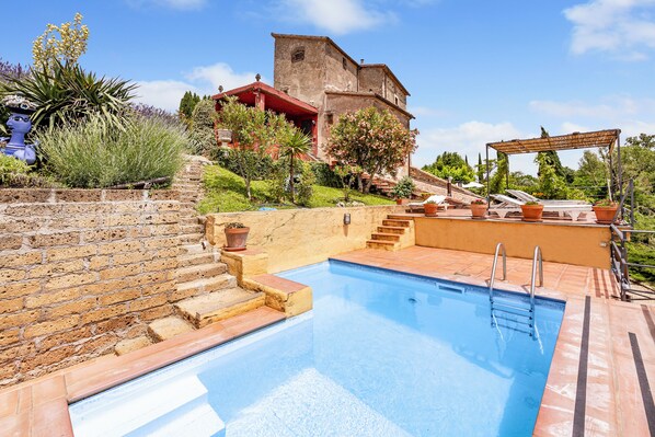 A swimming pool with steps leading to a house with a red roof, surrounded by greenery and a clear sky. - Torre Del Melograno With Heated Pool (Castiglione in Teverina)