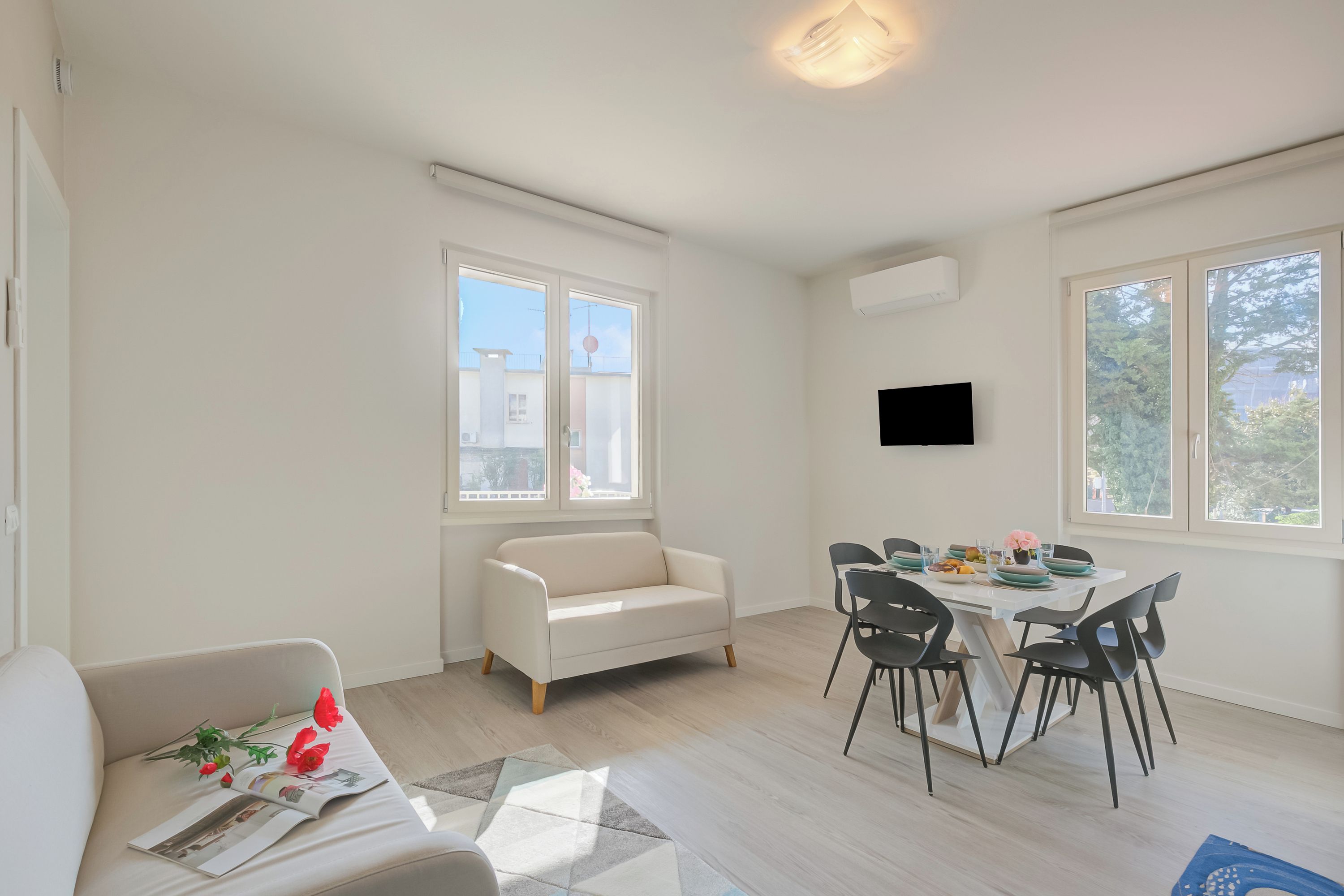Een moderne woonkamer met een bank, eettafel, stoelen en een flatscreen televisie die aan de muur hangt.