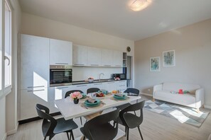 Et moderne køkken med hvide skabe, et spiseområde med et bord dækket til to, og en hvid sofa i opholdsstuen.