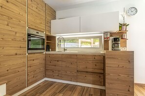A modern kitchen with wooden cabinetry, a built-in oven, and a window above the sink.