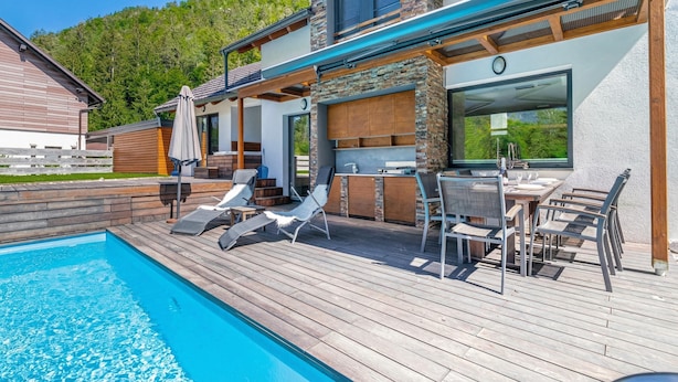 Et moderne hus med swimmingpool, udendørs møbler og en pejs i sten.