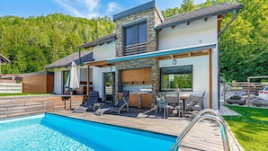 Et moderne hus med swimmingpool, udendørs siddepladser og udsigt til et skovområde.