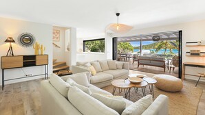 A modern living room with a sofa set, a coffee table, and a dining area. There is a view of the outdoors through large windows. - A dream villa for an unforgettable vacation! (Cul-de-Sac)