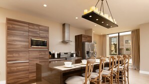 Een moderne keuken met houten kastjes, een centraal eiland met stoelen, een roestvrijstalen koelkast en een inbouwmagnetron.