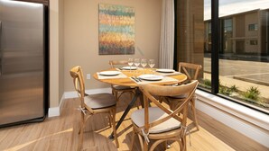 Een moderne eethoek met een houten tafel voor vier personen, omringd door houten stoelen met beklede zitplaatsen. Een groot raam biedt uitzicht op buiten.