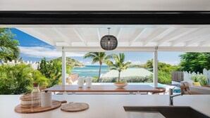 A modern outdoor dining area with a view of the ocean and palm trees. - A dream villa for an unforgettable holiday! (SAINT MARTIN)