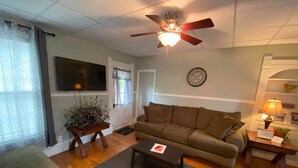 A living room with a sofa, a coffee table, a TV, a ceiling fan, a clock, and a lamp. - White House Lodge-Lower Studio (Brookfield)