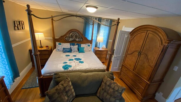 A four-poster bed with floral bedspread, a wooden wardrobe, and a green sofa with patterned cushions. - White House Lodge-Lower Studio (Brookfield)