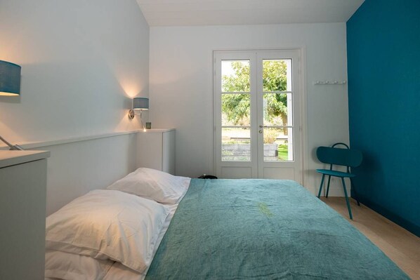 A bedroom with a bed, a chair, a desk, and a window with a view of greenery. - Rialto - Magnificent architect's house sea view (Les Portes-en-Ré)