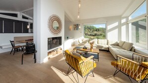 A spacious living area with a sofa, coffee table, and chairs, a dining area with a table and chairs, and a kitchen with cabinets and a fireplace. - Rialto - Magnificent architect's house sea view (Les Portes-en-Ré)