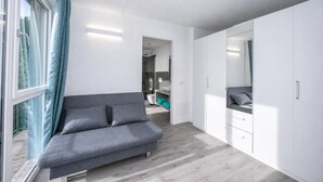 Un dormitorio moderno con un sofá gris, un armario blanco y vistas a través de una ventana.