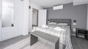 Un dormitorio con cama, mesitas de noche, un banco, un armario y un equipo de aire acondicionado.