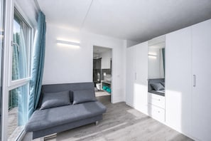 A modern bedroom with a grey sofa, white wardrobe, and a view through a window. - Rustichel Fantastic Lake View (Toscolano Maderno)