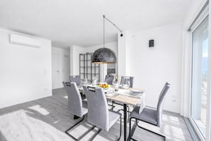 A modern dining room with a geometric pendant light, a white air conditioner, and a view through a large window. - Rustichel Fantastic Lake View (Toscolano Maderno)