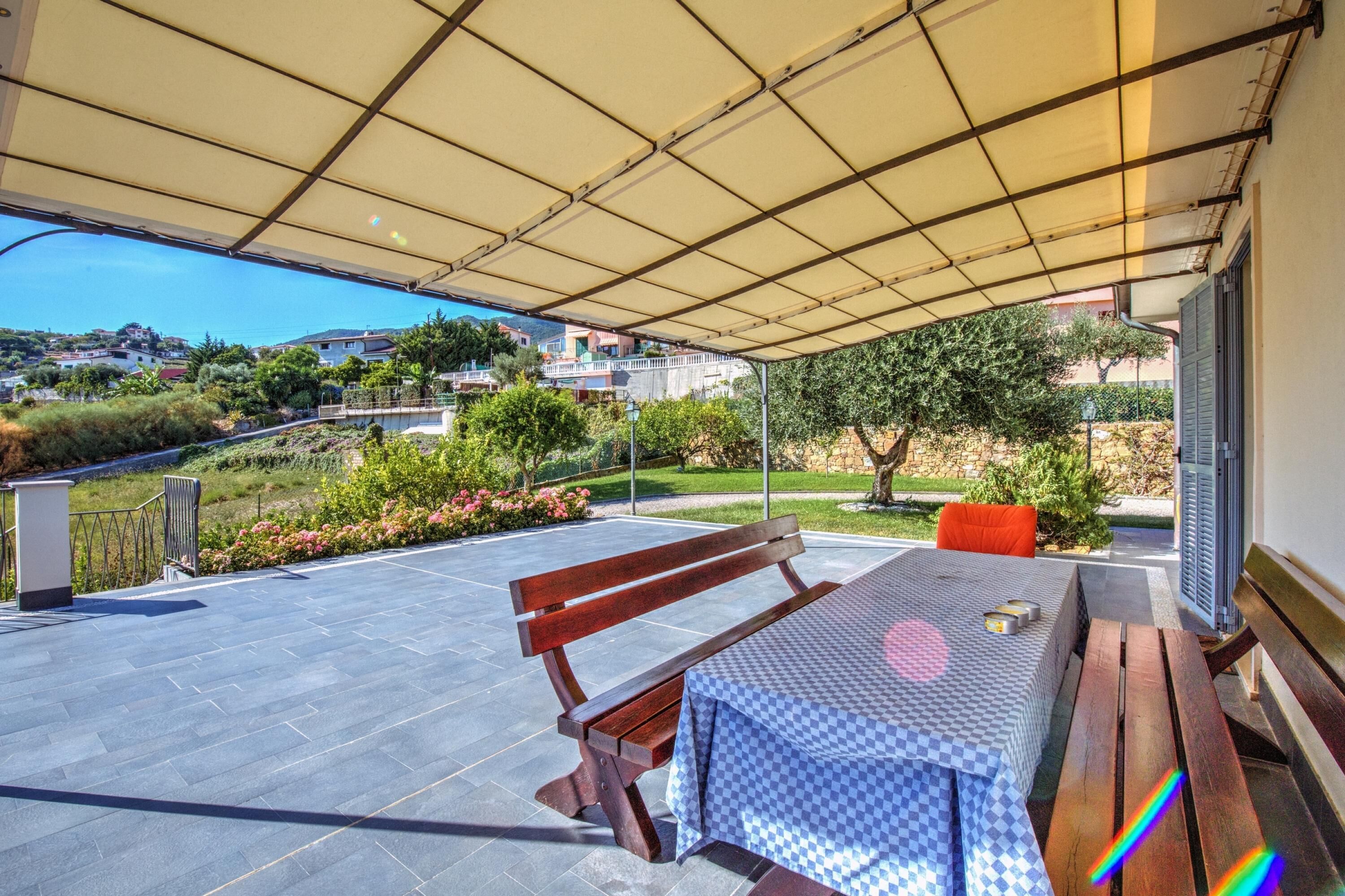Un patio exterior con una mesa y un banco, un área cubierta y vistas a una zona residencial.