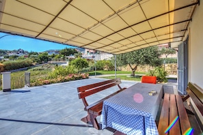 Un patio exterior con una mesa y un banco, un área cubierta y vistas a una zona residencial.