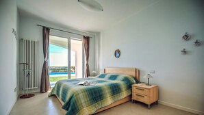 Un dormitorio con cama, mesita de noche, lámpara y vistas a través de una ventana.