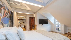 A bedroom with a bed, a TV mounted on the wall, a window, and a staircase leading to another room. - Tromostovje In Heart Of Ljubljana (Ljubljana)